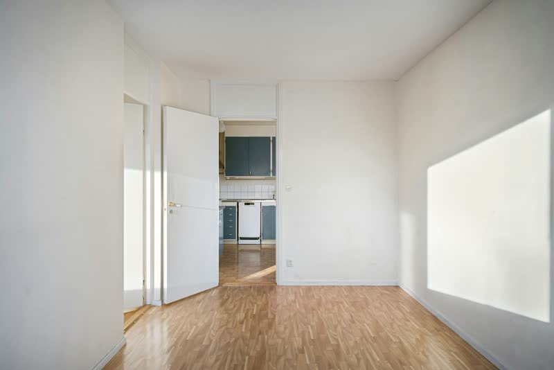 Leeres Zimmer mit Parkettboden, die offene Tür gibt den Blick in die Küche frei